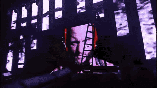 a man 's face is projected on a wall with a ladder in the background