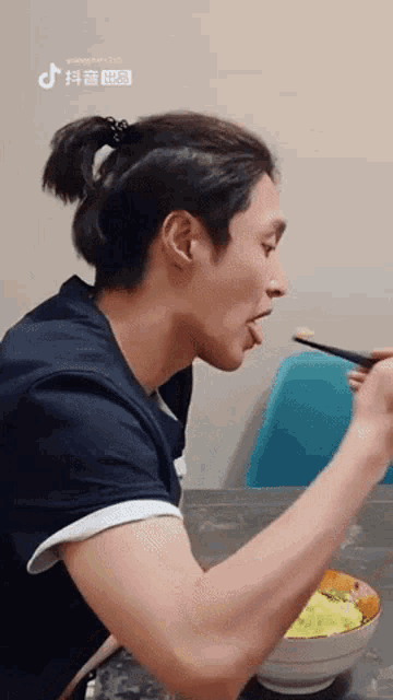 a man with a ponytail is eating a bowl of food with chopsticks .