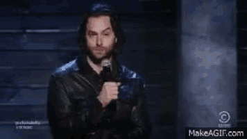 a man in a leather jacket is standing in front of a microphone on a stage .