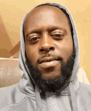 a man with a beard is wearing a grey hoodie and making a funny face .