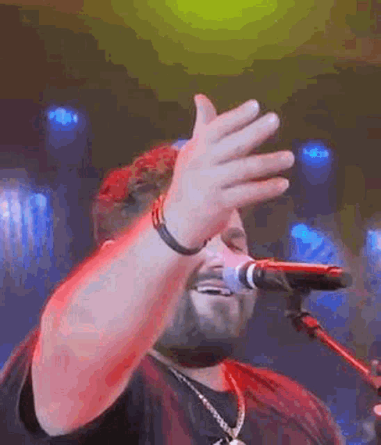 a man is singing into a microphone while covering his face with his hands .