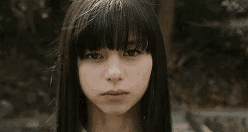 a close up of a woman 's face with long hair and bangs looking at the camera .