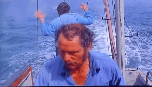 a man in a blue shirt is walking on a boat in the ocean