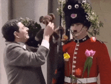 a man in a red uniform is holding a teddy bear next to a man in a black hat