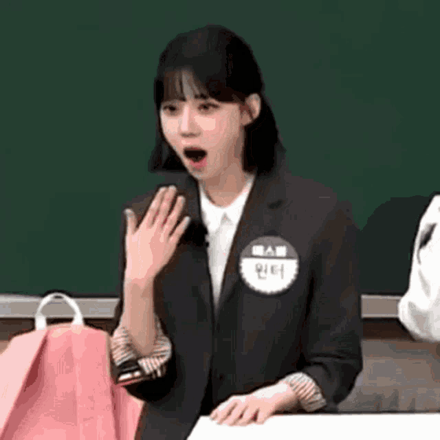 a woman in a suit is standing in front of a blackboard with her mouth open .