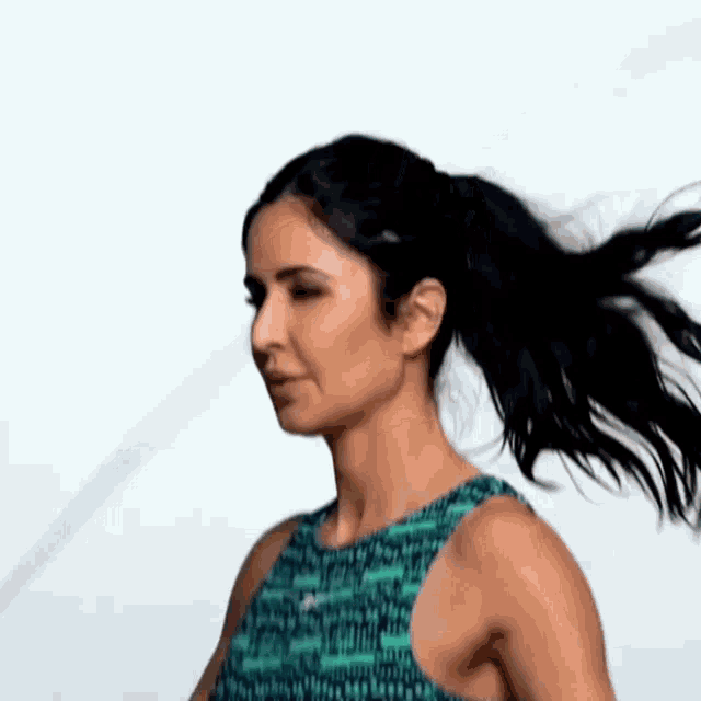 a woman with long black hair is wearing a ponytail and a blue tank top .