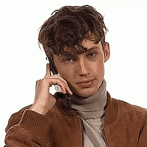 a young man is talking on a cell phone while wearing a brown jacket and a turtleneck .