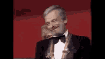 a man in a tuxedo is smiling in front of a red wall while wearing a medal around his neck .