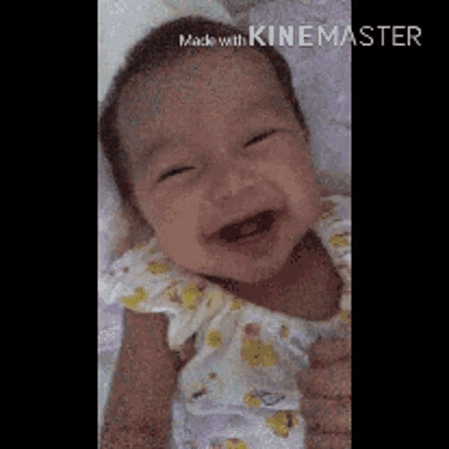 a baby is smiling while laying on a bed in a video made by kinemaster