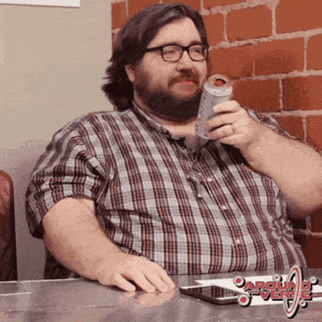 a man in a plaid shirt sits at a table with a can of soda in his hand