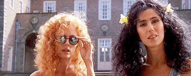 two women are standing in front of a building and one has a flower in her hair .