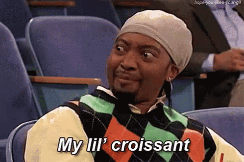 a man wearing a hat and sweater is sitting in a chair and says my lil ' croissant