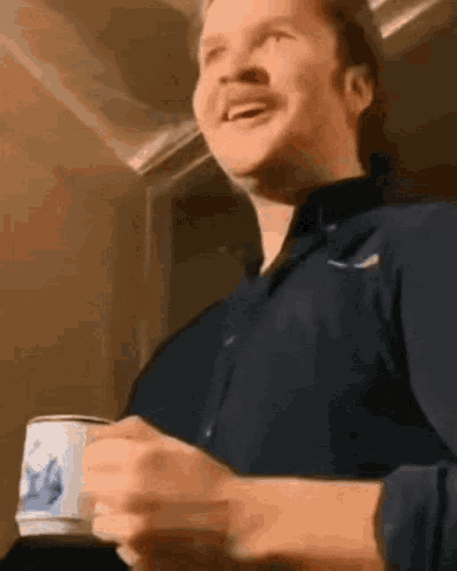 a man in a blue shirt is smiling while holding a cup of coffee