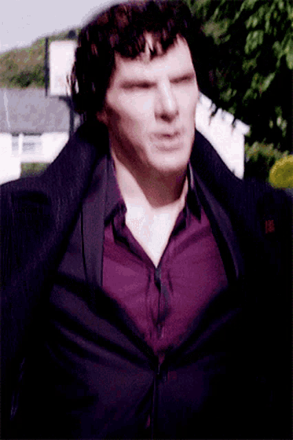 a man wearing a purple shirt and a black jacket looks at the camera