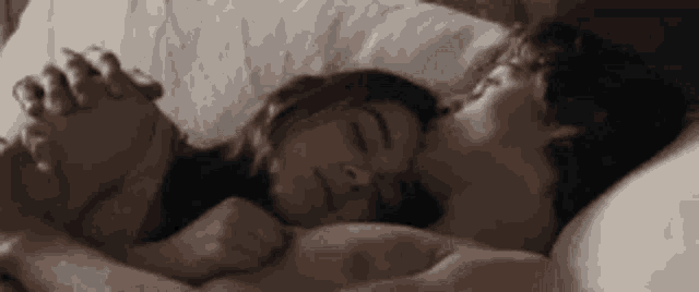 a man and a woman are laying in bed holding hands and hugging each other .
