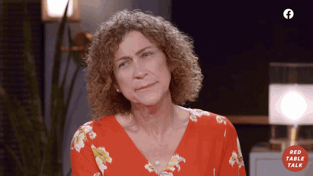 a woman in a red floral shirt is sitting in front of a red table talk sign