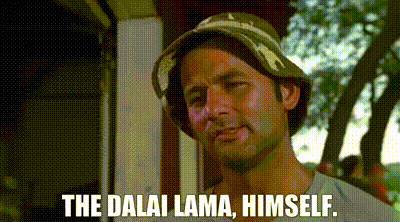 a man wearing a bucket hat is standing in front of a building and says `` the dalai lama , himself . ''