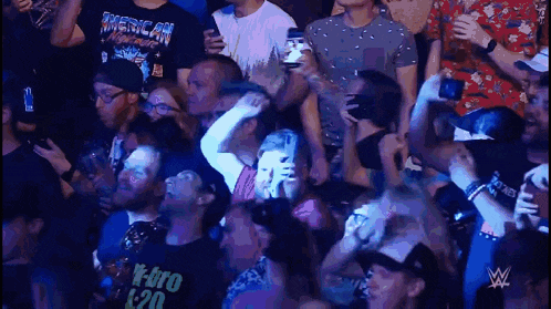 a crowd of people are watching a wrestling match on a television screen .
