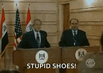 two men are standing at podiums with flags in the background and one of them is saying stupid shoes .