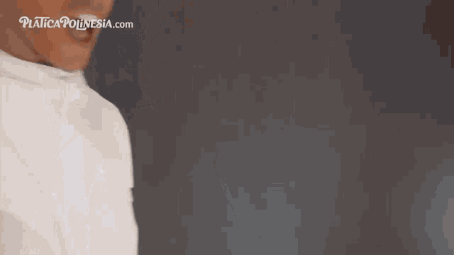 a man in a white shirt is standing in front of a black wall and making a funny face .