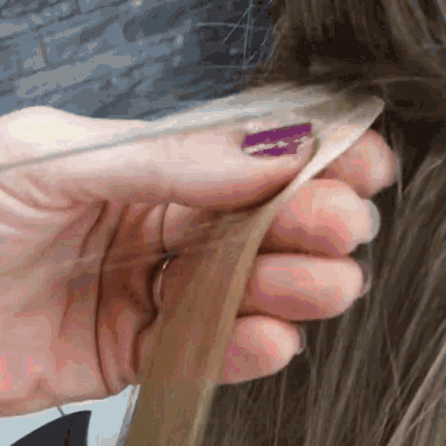 a woman with purple nails is holding a piece of hair .