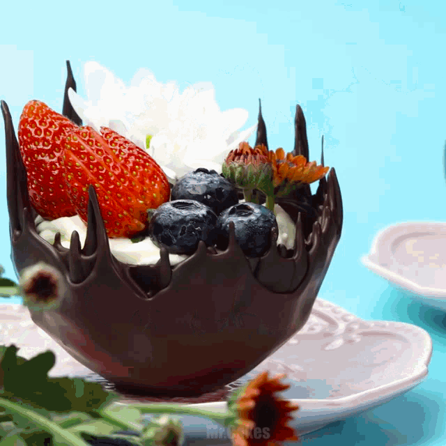 a chocolate bowl filled with strawberries and blueberries is on a plate