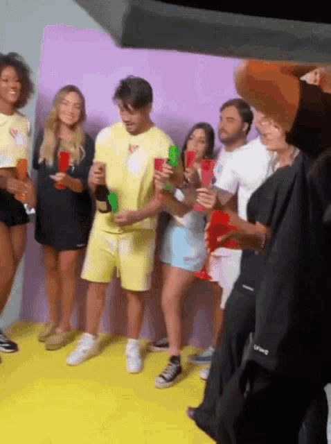 a group of people standing in front of a purple wall holding glasses and bottles