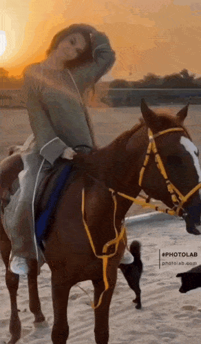 a woman is riding a horse on a sandy beach at sunset .