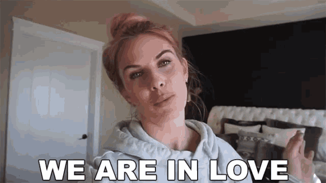 a woman is standing in front of a bed with the words `` we are in love '' written on it .