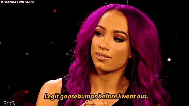 a man in a suit is sitting next to two women with purple hair . one of the women is holding a wrestling belt .