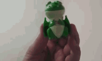 a person is holding a green frog toy in their hand .