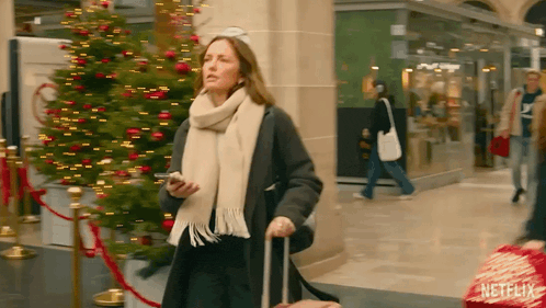 a woman with a suitcase is walking in front of a christmas tree and a netflix logo