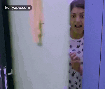 a woman is peeking out from behind a door holding a cell phone .
