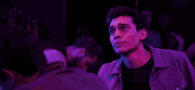 a man in a purple jacket is talking to another man in a nightclub .