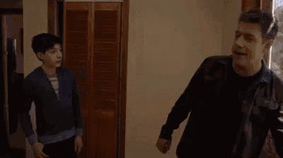 a man and a boy are standing in a hallway holding hands .