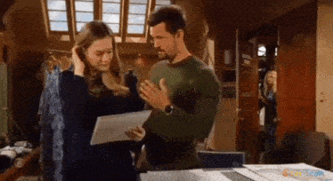 a man and a woman are standing next to each other and looking at a piece of paper .
