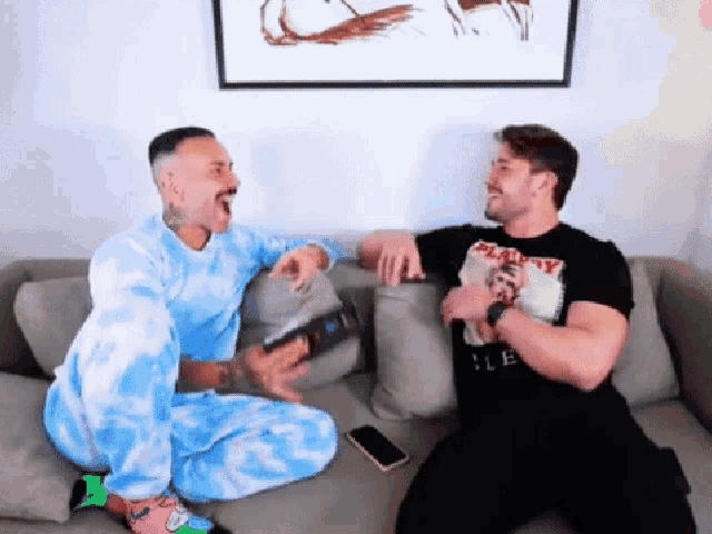 two men are sitting on a couch laughing and one is wearing a shirt that says heavy metal