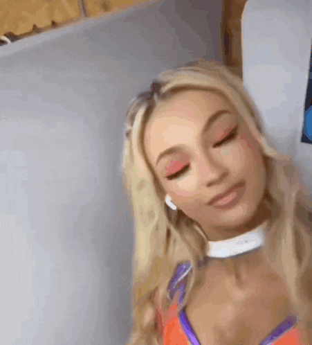 a blonde woman wearing headphones and a choker is sitting on a couch