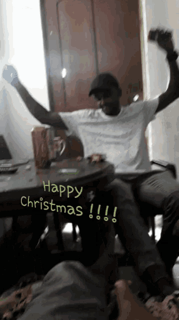 a man sitting at a table with his arms in the air and the words happy christmas below him