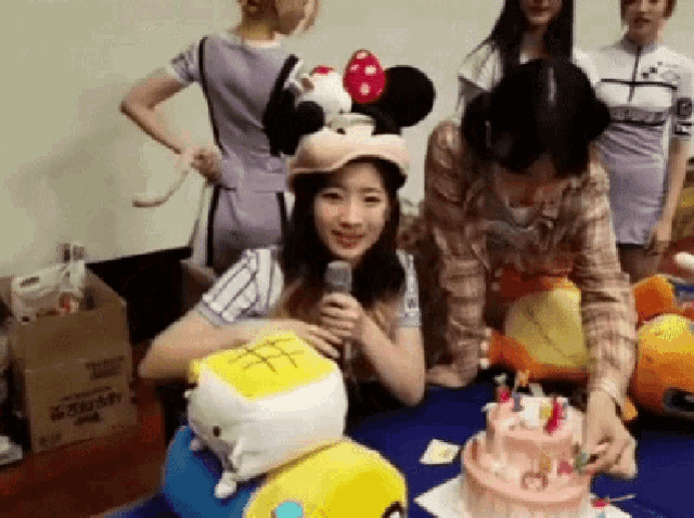 a woman wearing a mickey mouse hat is sitting at a table with a cake