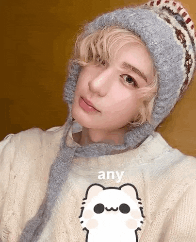 a woman wearing a hat and a sweater with a cat on it is taking a selfie .