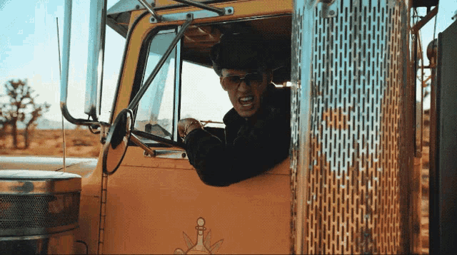 a man wearing sunglasses and a hat is driving a large truck