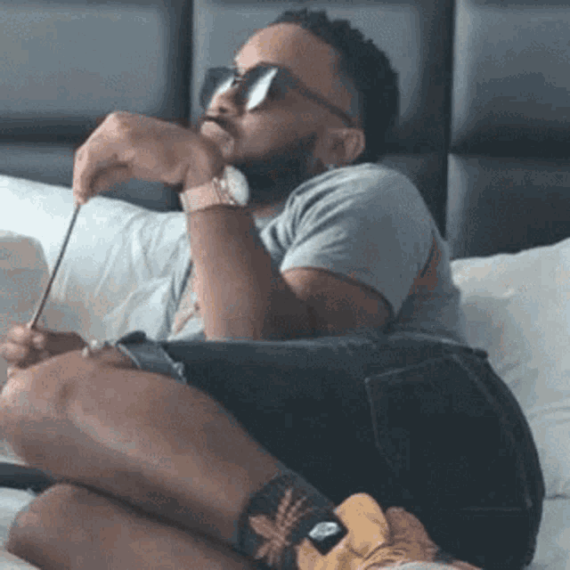 a man wearing sunglasses is sitting on a bed with his legs crossed .