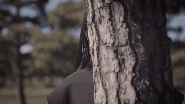 a woman with long hair is standing behind a tree .