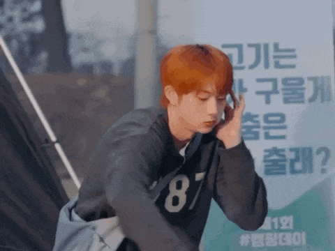 a young man with red hair is talking on a cell phone while standing in front of a sign .