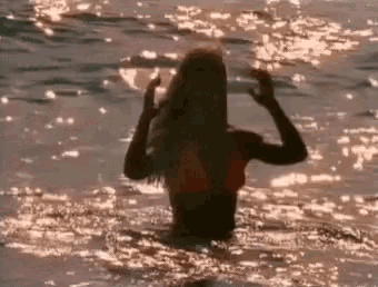 a woman in a bikini is standing in the ocean at sunset .