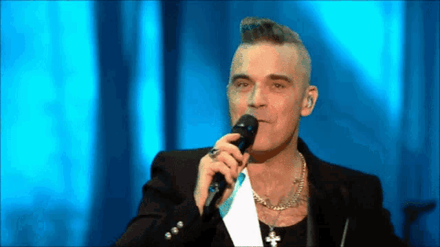 a man singing into a microphone in front of a blue background