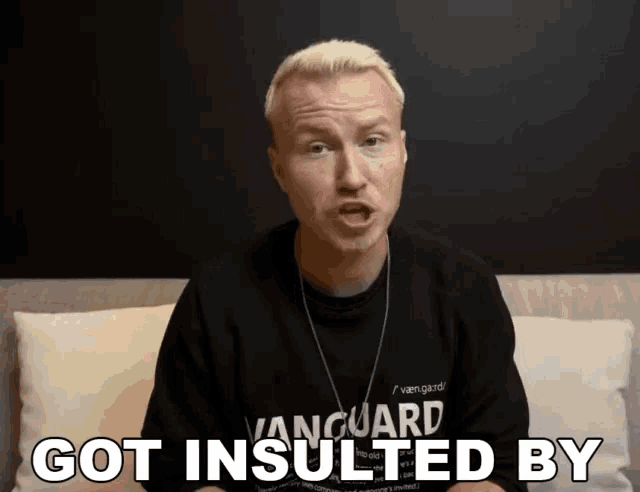 a man wearing a black vanguard sweatshirt is sitting on a couch