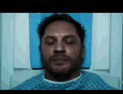 a man is laying in a hospital bed with his eyes closed and a beard .