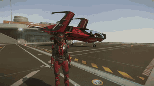 a man in a red suit stands on a runway in front of a red fighter jet